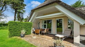 A house with a thatched roof, a patio with outdoor furniture, and a well-maintained garden.