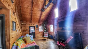 A cozy cabin interior with wooden walls, a ceiling fan, a fireplace, a rocking chair, and a bed with colorful bedding. - New River & Gauley River family cabin -10 minutes to state & national parks (Hico)
