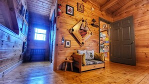 A cozy cabin interior with a wooden floor, a sofa with cushions, a wall-mounted fire extinguisher, a door, and various wall decorations. - New River & Gauley River family cabin -10 minutes to state & national parks (Hico)