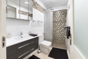 A modern bathroom with a white sink, dark vanity, a glass shower enclosure, and a tiled shower wall.