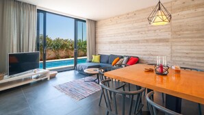 A modern living room with a large TV, a wooden dining table, and a pool view. - Awesome home in Sutivan (Sutivan)