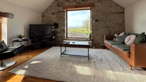 Un salon chaleureux avec un mur en pierre, une grande fenêtre, un téléviseur, un canapé et une table basse.