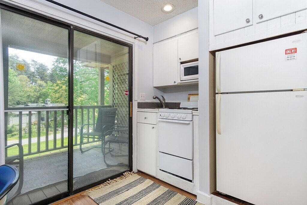 A kitchen with a sliding glass door leading to a balcony, a microwave, and a refrigerator.