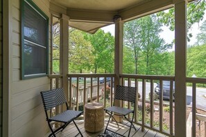 A covered porch with two chairs and a wicker basket, overlooking a road and trees.