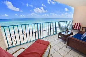 Ein Balkon mit Blick auf den Strand, eine Rattan-Couch, ein kleiner Tisch und eine rote Bank.
