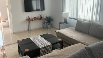 Un salon avec un canapé, une table basse, un téléviseur et un ventilateur de plafond.
