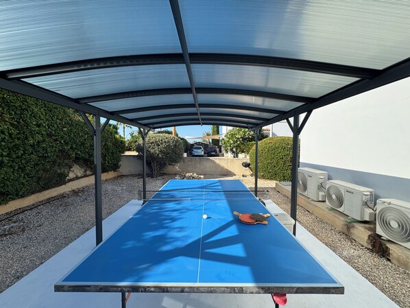 Mesa de ping pong al aire libre bajo una zona cubierta, con vistas despejadas del paisaje circundante.