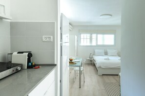 A modern kitchen with a built-in stove, a small dining table with chairs, and a bed with white bedding in the adjacent room. - CozyStudio Apt in a vibrant neighborhood (Tel Aviv)