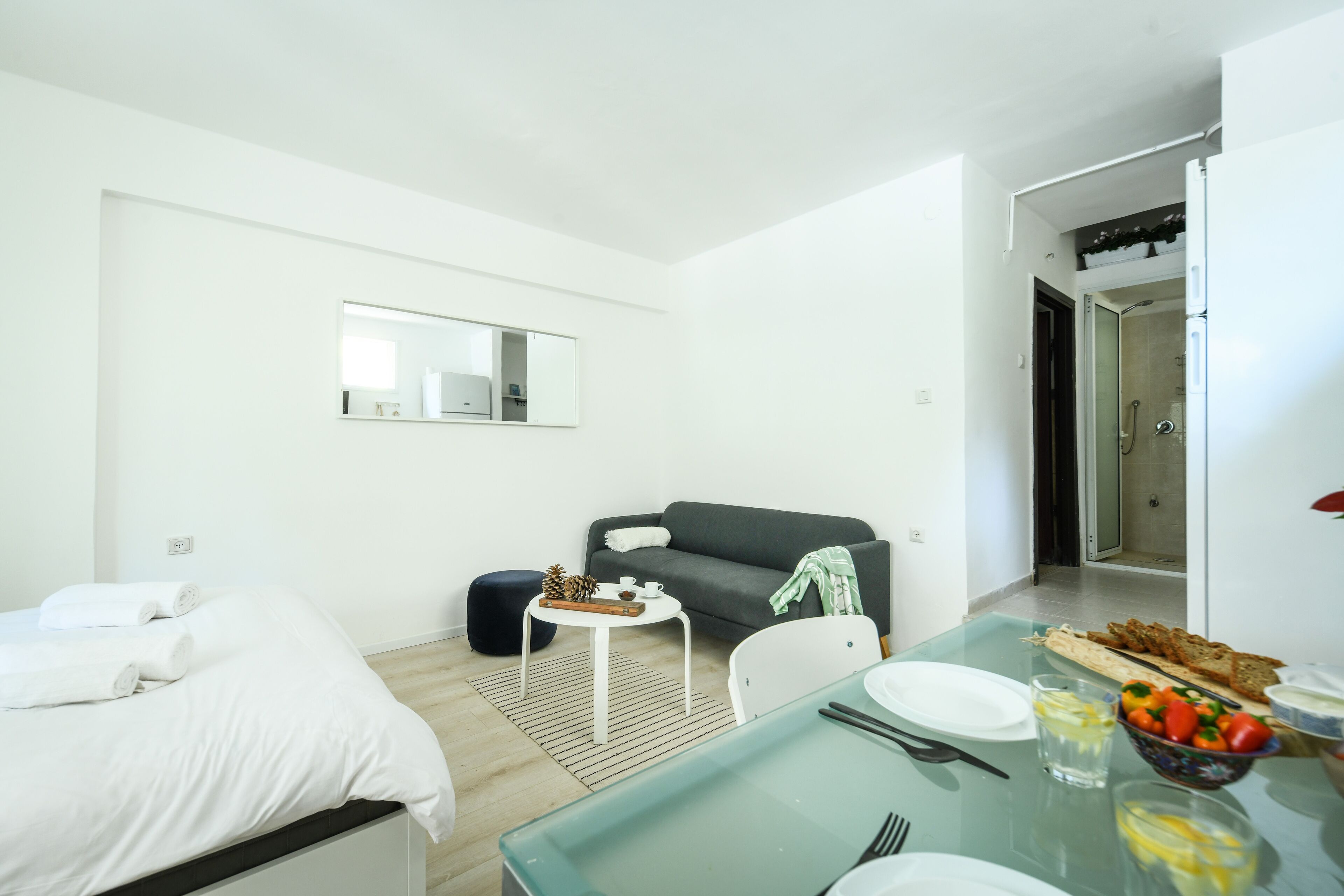 A modern hotel room with a bed, a sofa, a dining table with breakfast items, and a shower area.
