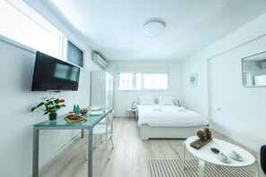 A modern hotel room with a bed, a TV, a desk with a plant, and a small table with cups and a pine cone. - CozyStudio Apt in a vibrant neighborhood (Tel Aviv)