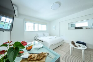 A modern hotel room with a bed, a dining table with breakfast, a TV, and a window. - CozyStudio Apt in a vibrant neighborhood (Tel Aviv)