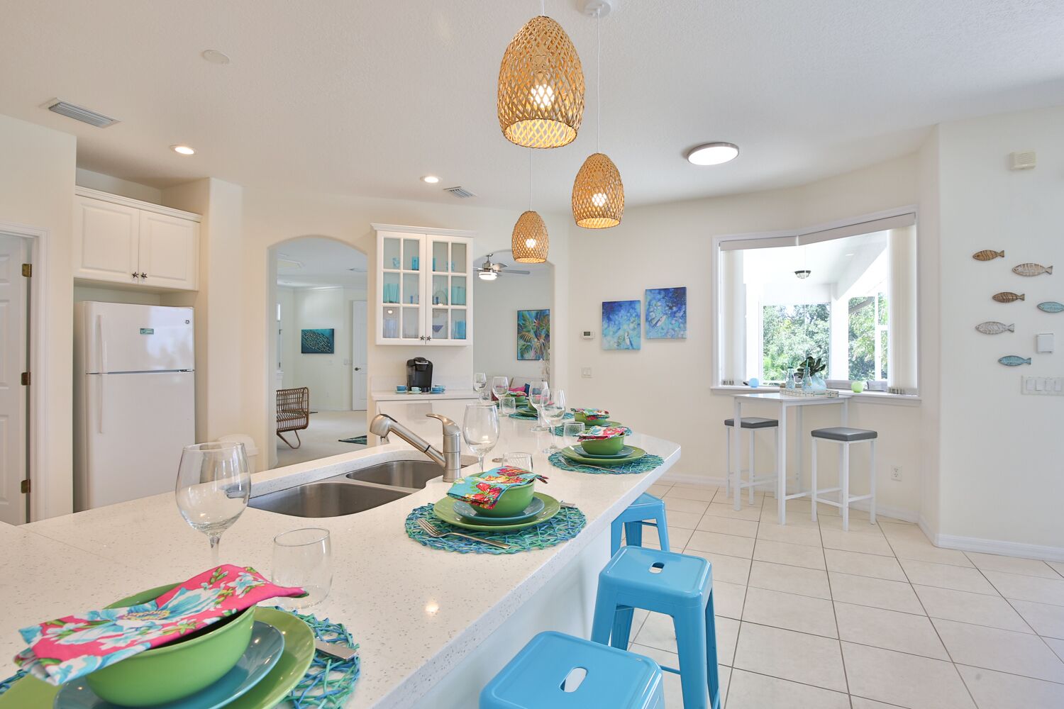 Una cocina moderna con armarios blancos, una isla central con taburetes azules e iluminación colgante.