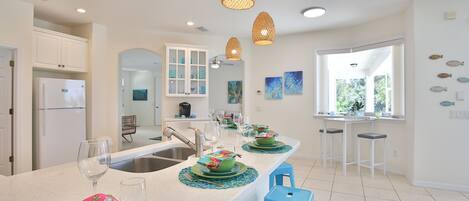 Una cocina moderna con armarios blancos, una isla central con taburetes azules e iluminación colgante.