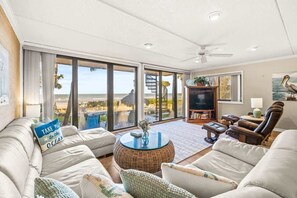 A spacious living room with a large sliding glass door leading to a balcony, a comfortable sofa set, a television, and a dining area. - Concha 5 in Belleair Beach! (Belleair Beach)