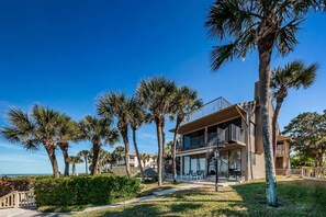 A two-story building with a balcony, surrounded by palm trees and a clear sky.