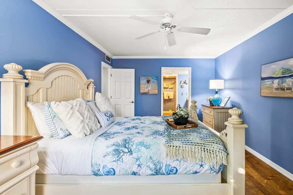 Ein Schlafzimmer mit einem Bett, einem Deckenventilator, einer Tür und einer Wand mit einem Gemälde.