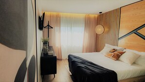 Et moderne hotelværelse med en seng, et sengebord med en vase og et vægmonteret fjernsyn.