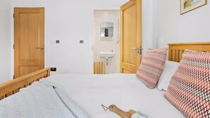 Ein Schlafzimmer mit Bett, Holz-Kopfteil, Nachttisch, Spiegel, Waschbecken und einer Tür.