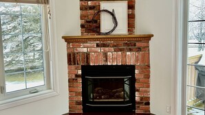 A corner room with a brick fireplace, wooden flooring, and a view of trees through a window. - Luxurious Getaway - Near Sandbanks and Wineries (Picton)