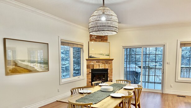 A dining room with a wooden table, chairs, a fireplace, and large windows with a view of snow-covered trees. - Luxurious Getaway - Near Sandbanks and Wineries (Picton)