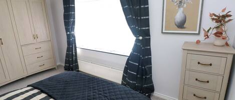 Un dormitorio con cama, armario, radiador, ventana con cortinas e imagen enmarcada en la pared.