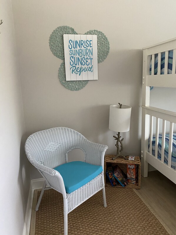 A baby room with a white wicker chair, a crib, a wall decoration, and a box of Jenga. - 3 BR, 2 Bath home in Emerald Isle! Golf cart, beach chairs & Shibumi included! (Emerald Isle)