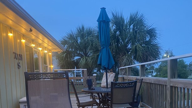 A wooden deck with outdoor seating, a fire feature, and a blue umbrella. - 3 BR, 2 Bath home in Emerald Isle! Golf cart, beach chairs & Shibumi included! (Emerald Isle)