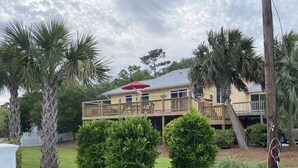 A two-story house with a balcony, surrounded by palm trees and a white picket fence. - 3 BR, 2 Bath home in Emerald Isle! Golf cart, beach chairs & Shibumi included! (Emerald Isle)