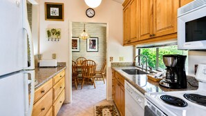 Una cocina con gabinetes de madera, microondas, cafetera y comedor con sillas y mesa.