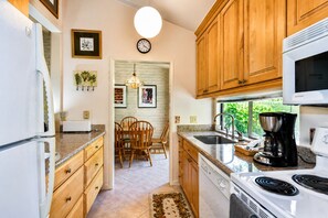 A kitchen with wooden cabinets, a microwave, a coffee maker, and a dining area with chairs and a table. - Perfect Wine Country Retreat at Silverado (Napa)