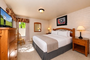 A hotel room with a bed, wooden nightstands, a dresser, a mirror, and a television.