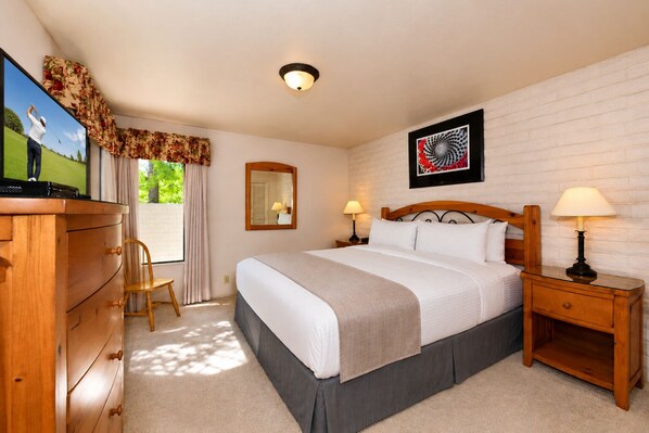 A hotel room with a bed, wooden nightstands, a dresser, a mirror, and a television.
