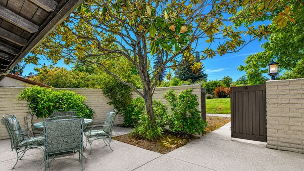 Un patio con mesa y sillas, un árbol y una verja.