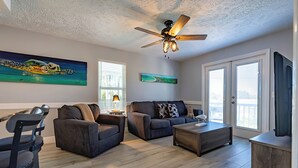 A spacious living room with a ceiling fan, two sofas, a coffee table, and a TV. - TranquiliSea: Pet friendly, long term discount, resort-style pool! (Holmes Beach)
