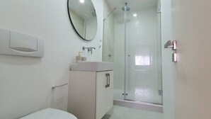 Une salle de bain comprenant des toilettes, un lavabo, un miroir et une douche fermée par une paroi de verre.