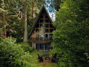 A cabin with a stone facade, wooden balcony, and surrounded by dense forest. - Spacious North Cascades Riverside A-Frame w/ Mt Baker Views - Dog-Friendly (Concrete)