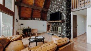 Uma sala de estar espaçosa com lareira de pedra, sofás de couro e teto de madeira.