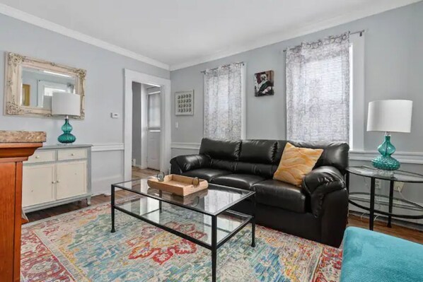 Un salon avec un canapé en cuir noir, une table basse en verre, un meuble blanc et un tapis à motifs.