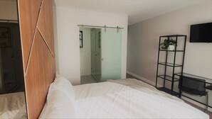 Une chambre à coucher avec un lit, une armoire, un téléviseur fixé au mur et une plante posée sur une étagère.