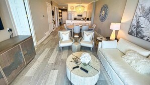 A spacious living area with a sofa, coffee table, and chairs. A kitchen is visible in the background. - Exquisite Beach Condo, Comfortable, Luxurious, Beachfront, Free Beach Service (Panama City Beach)