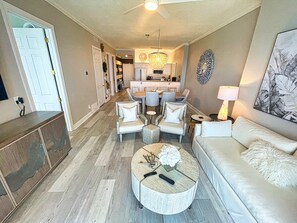 A spacious living area with a sofa, coffee table, and chairs. A kitchen is visible in the background. - Exquisite Beach Condo, Comfortable, Luxurious, Beachfront, Free Beach Service (Panama City Beach)