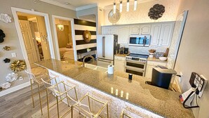 A modern kitchen with a granite countertop, stainless steel appliances, and a bar area with gold chairs. - Exquisite Beach Condo, Comfortable, Luxurious, Beachfront, Free Beach Service (Panama City Beach)