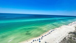 A beach with clear turquoise water, a sandy shore, and a row of blue umbrellas. - Exquisite Beach Condo, Comfortable, Luxurious, Beachfront, Free Beach Service (Panama City Beach)