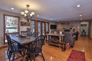 Un salon spacieux doté d’une cheminée, un coin repas avec des meubles en bois et de grandes fenêtres offrant une vue sur un lac.