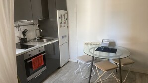 Kompakti keittiö, jossa on jääkaappi, pesuallas ja liesi. Siellä on myös pieni ruokapöytä ja kaksi tuolia.