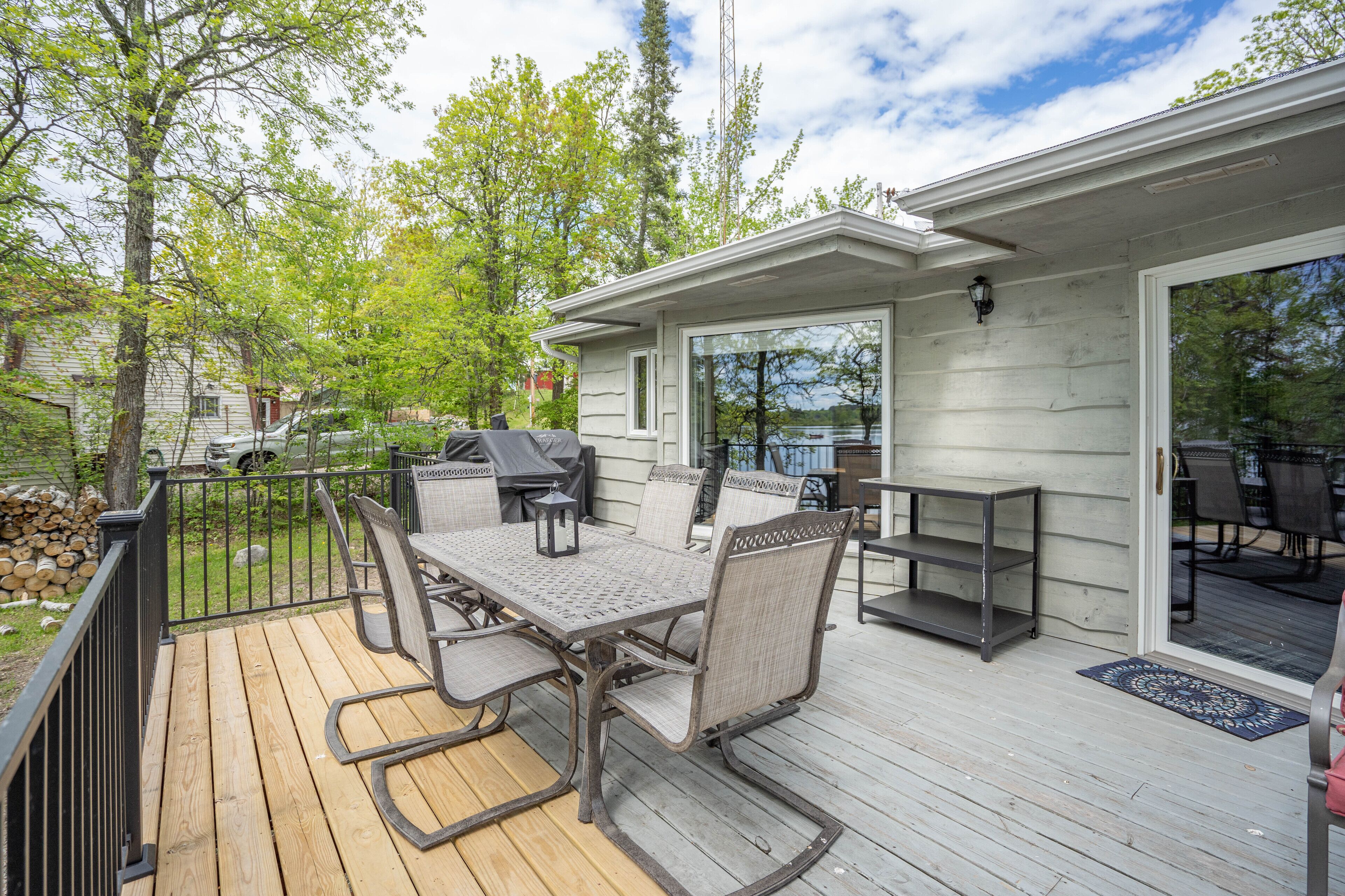 Une terrasse en bois avec une table et des chaises, un barbecue et un patio couvert offrant une vue sur le lac.