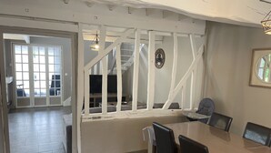 Un coin repas avec une table et des chaises, un téléviseur en arrière-plan et un escalier menant à une autre pièce.