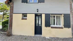Une maison à deux étages avec une porte noire, deux fenêtres avec des volets et un petit porche.