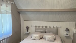 Une chambre à coucher avec un lit, deux tables de chevet, un luminaire au plafond et une fenêtre avec des rideaux.