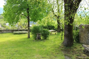 A grassy outdoor area with trees, a stone wall, and a picnic table. - "Le gîte de la glycine," a renovated house with a terrace offering a magnificent view and a fenced-in garden (Palmas d'Aveyron)